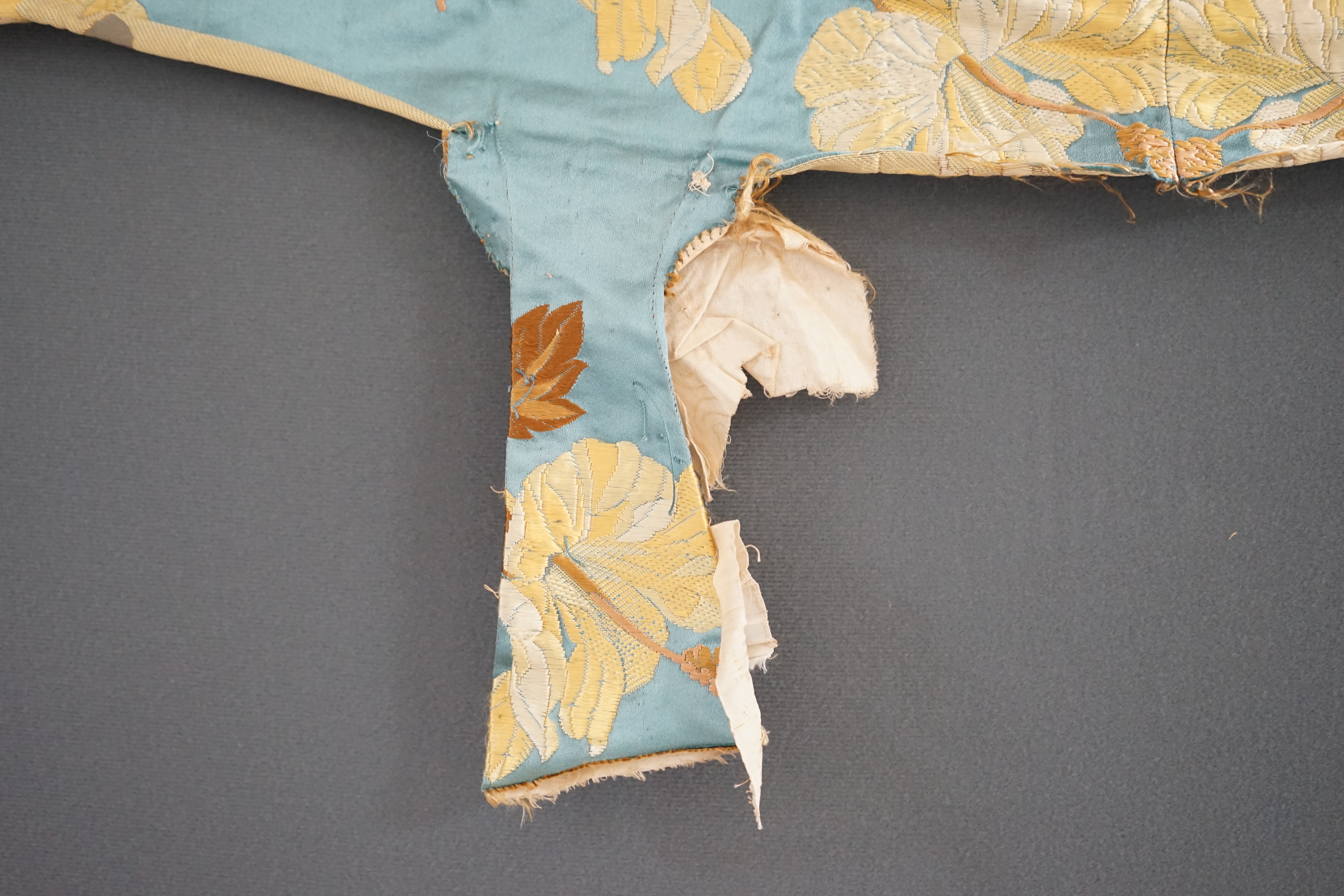 A turquoise satin floral silk brocaded panel of four 59cm widths, boldly embroidered in yellow and brown strays of lilies, the panel possibly part of a pelmet or half tester bed, each spray being 21cm high as a diagonal